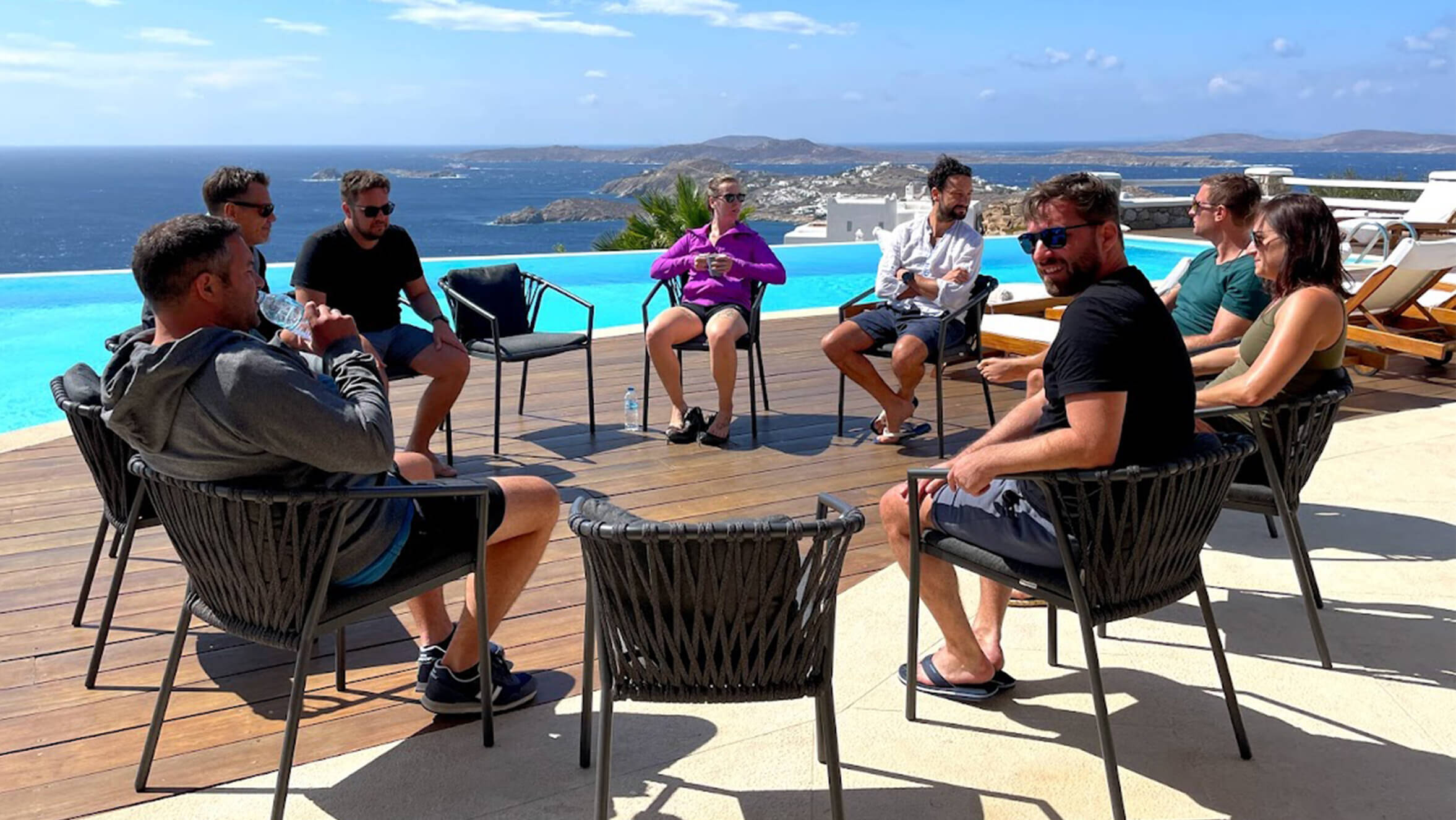 Eine Gruppe Männer und Frauen die vor einem Pool in einem Kreis aus Stühlen sitzen